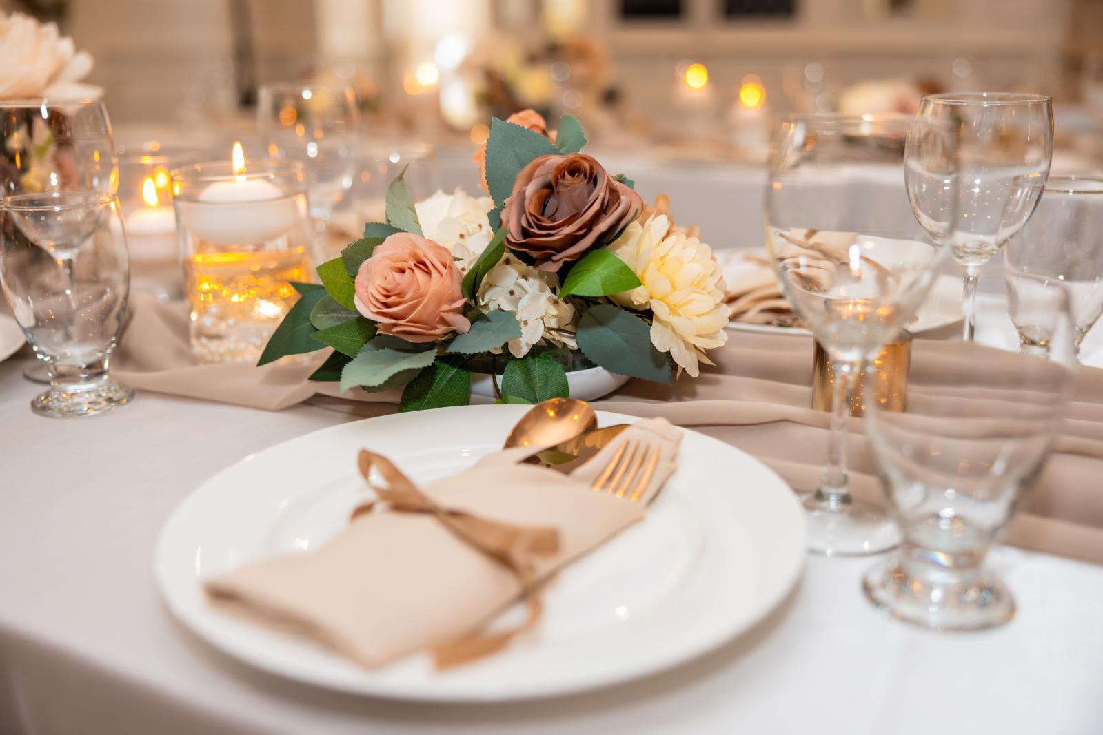 Elegant table close-up with neutral rose, gold flatware, and ambient lighting.